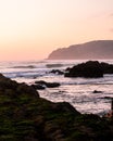 Pink sunset sky, beautiful ocean, sand  and green rocks. Portuese beach Royalty Free Stock Photo