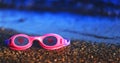 Pink swimming glasses on the sand with the red hearts on the len