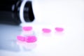 Pink tablet pills on blurred background of opened cap amber bottle on white background. Expired medicine. Drug degradation