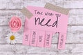 Pink tear-off stub note with text `Take what you need` and words `Love, Freedom, Hope, Courage` and `Strength` onwooden background