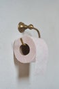 Pink toilet paper hanging on a gold toilet paper holder on a light bathroom wall Royalty Free Stock Photo