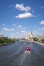 Pink tour boat is moving fast down the Moscow river on hot summer sunny day. Kotelnicheskaya skyscraper in background.