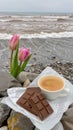 Pink tulips in a flowerpot sit next to a cup of coffee on the beach Royalty Free Stock Photo