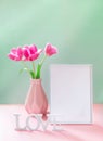 Pink tulips in vase, empty white frame, white letters LOVE on pastel pink green backdrop. Mock up. Royalty Free Stock Photo