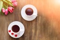 Pink tulips on wooden background, two cups of tea and coffee on saucers with hearts marmalade