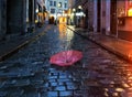 Pink umbrella on wet pavement at rainy medieval evening street light plurred reflektion rain fall in Tallinn old town Estonia