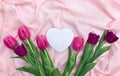 Pink, violet tulips on background of pink linen cloth with white paper card note in the shape heart with space for text. Top view Royalty Free Stock Photo