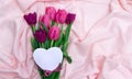 Pink, violet tulips on background of pink linen cloth with white paper card note in the shape heart with space for text. Royalty Free Stock Photo