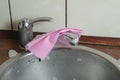 A pink viscose dish cloth rests on top of the kitchen faucet