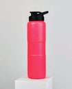 A pink water bottle with a black lid and a fliptop spout sits on a white platform against a white backdrop Royalty Free Stock Photo