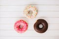 Pink, white and brown chocolate donuts laying on the white wooden table