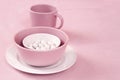 Pink and white crockery with sugar dragees inside on a pink cloth background