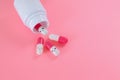 Pink white pills fall out of the bottle close up on pink background