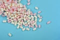 Pink and white marshmallow weets spilling out of glass container on blue background Royalty Free Stock Photo