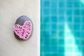 Pink wooden heart and stone on swimming pool edge with space on blurred blue water background Royalty Free Stock Photo