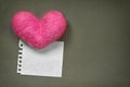 Pink wool toy heart lying with a clean notepad sheet on the grey paper background Royalty Free Stock Photo