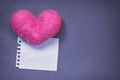 Pink wool toy heart lying with a clean notepad sheet on the violet paper background Royalty Free Stock Photo