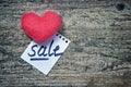 Pink wool toy heart lying with a notepad sheet with a word sale written on it on a wooden desk