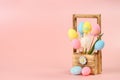 Pink, yellow and blue painted eggs on sticks and white tulip in a wooden basket for flowers on a pink background. Easter concept, Royalty Free Stock Photo