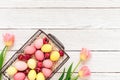 Pink and yellow easter eggs in basket with tulip flowers on white wooden background. Spring concept. Top view, copy space Royalty Free Stock Photo