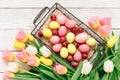 Pink and yellow easter eggs in basket with tulip flowers on white wooden background. Spring concept. Top view Royalty Free Stock Photo