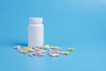 Pink and yellow pills, tablets and white bottle on blue background Royalty Free Stock Photo