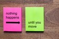 Pink and yellow self-adhesive note sticker with the motto: nothing happens until you move. Background dark wooden table