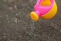 A pink yellow watering can water the ground. Drops of water spill, dissipate moisturize the earth. Help fight the drought. Royalty Free Stock Photo