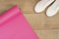 Pink yoga mat and white trendy sneakers on a wooden background. Fitness concept, active lifestyle, body care concept. Wood Backgro