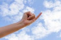 A pinkie and hand reaching toward the blue sky background.