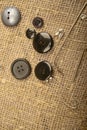 Pins of different sizes and different buttons on the burlap with a rough texture. Close up