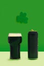 A pint of black stout beer glass and beer can standing alone in front of green clover above. Lucky pub minimal concept Royalty Free Stock Photo