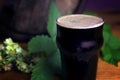 Pint of dark beer foam beautifully on a barrel with a leaf of hops background Royalty Free Stock Photo