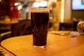 Pint glass of dark stout beer with foam stands on a wooden table in a bar Royalty Free Stock Photo