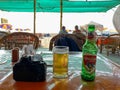 A pint of Kingfisher beer in a mug next to a Nikon DSLR camera at a beach shack in Calangute