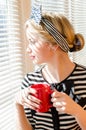 Pinup girl blond contemplating beautiful young woman with a red cup looking wistfully out the window portrait Royalty Free Stock Photo