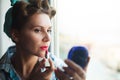 Pinup look dressed woman paints her lips with red lipstick