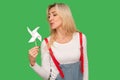 Pinwheel toy. Portrait of beautiful adult woman in stylish overalls blowing at paper windmill, playing with origami Royalty Free Stock Photo