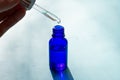 Pipette of blue glass bottle full of face serum on blue background on bright sunlight.