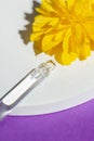 Pipette with serum or cosmetic liquid close-up on a podium with yellow flowers on purple background. Royalty Free Stock Photo