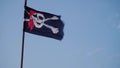 Pirate flag on flagpole evolving in the wind against a blue sky