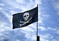 pirate flag jolly roger skull and bones in front of blue cloudy sky Royalty Free Stock Photo