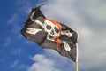 Pirate flag `Jolly Roger` on a background of blue sky with clouds on a bright sleepy day. Royalty Free Stock Photo