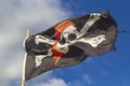 Pirate flag `Jolly Roger` on a background of blue sky with clouds on a bright sleepy day. Royalty Free Stock Photo