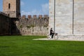 Woman biking next to the ancient walls of Pisa and Monumental Cemetery at the Square of Miracles in a