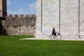 Woman biking next to the ancient walls of Pisa and Monumental Cemetery at the Square of Miracles in a