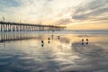 Historical wooden Pismo Beach pier at sunset. Wide sandy beach with beautiful sun reflections, birds, and cloudy sky on background Royalty Free Stock Photo