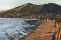 Pismo beach cliffs, wide sandy beach at low tide, green hills, and silhouette of a town in the background at sunset, California