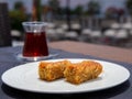Pistachio kadayif on white plate with turkish tea on table in outdoor cafe.