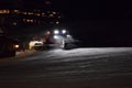 A snow groomer compacting ski runs at night